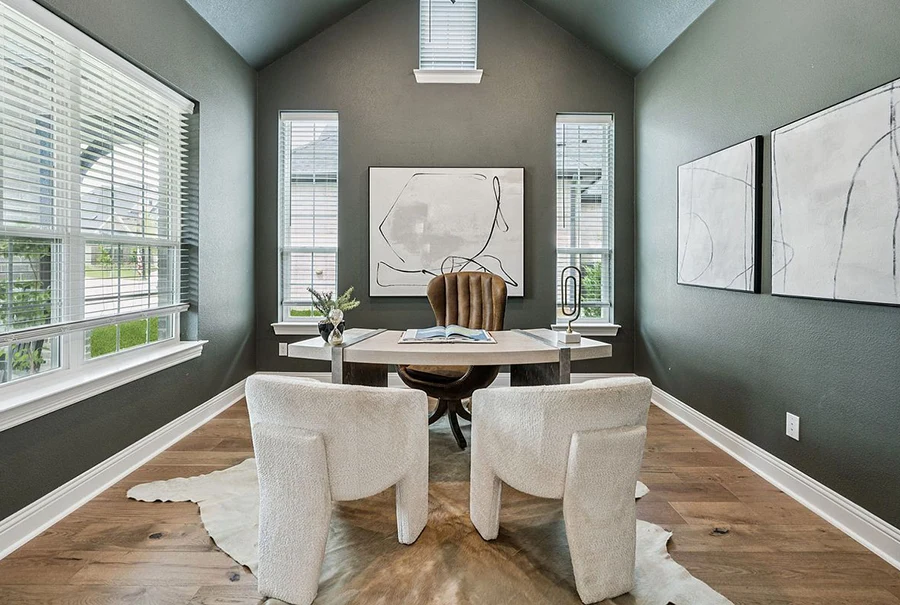 Large study with green walls and wood floor, modern desk, large leather desk chair, two white guest chairs and rawhide rug