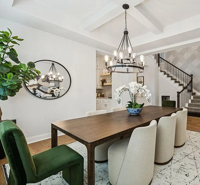 Dining room with large wood rectangle table, two green velvet end chairs, six white round low back side chairs, large black lighting.