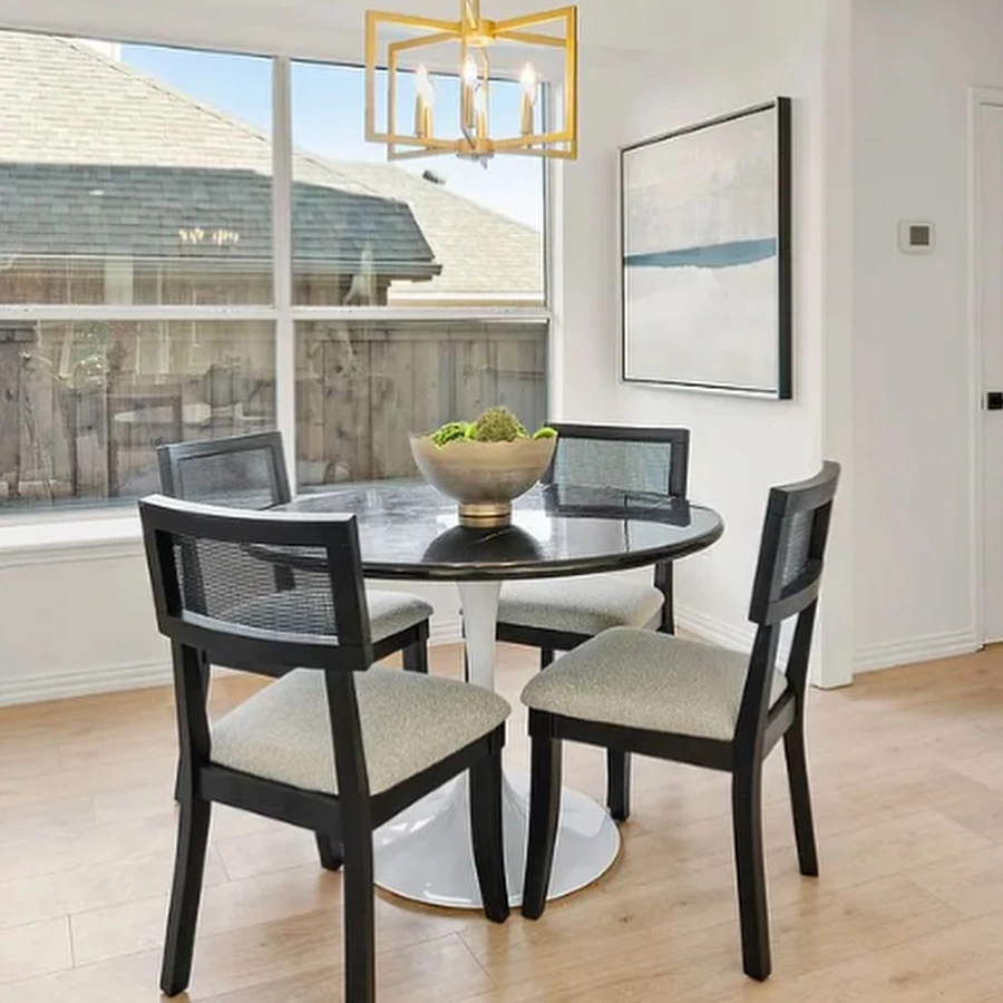 Small dining area staged with a round white and black table, four black wooden chairs with white cushions, black and grey artwork