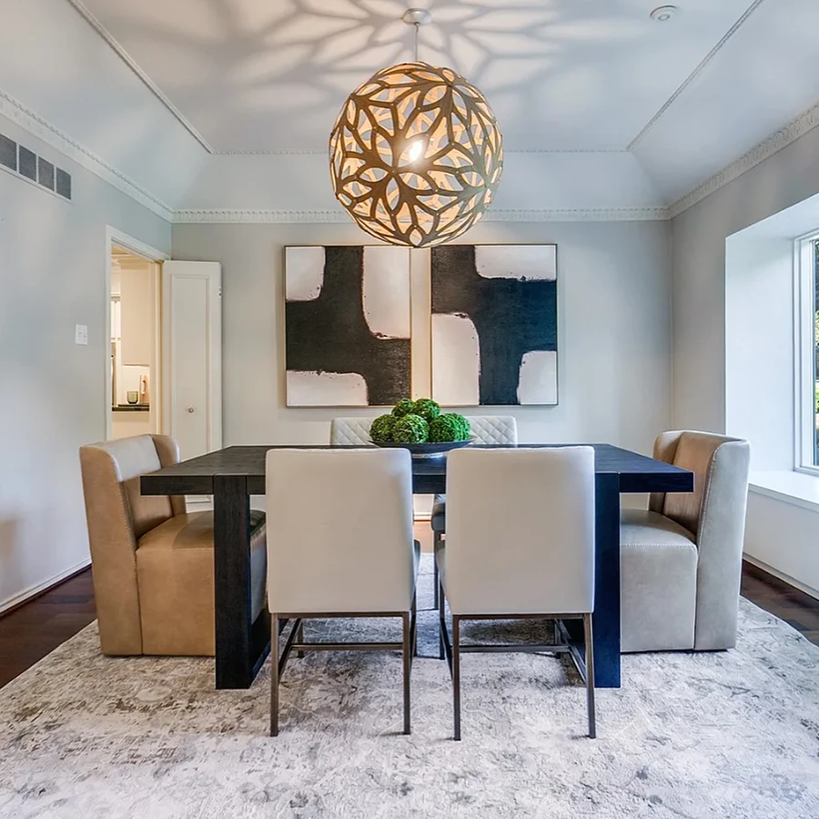 Dining room with large black wooden table, two leather end chairs and four white leather side chairs, a large round hanging light over the table and black and white artwork
