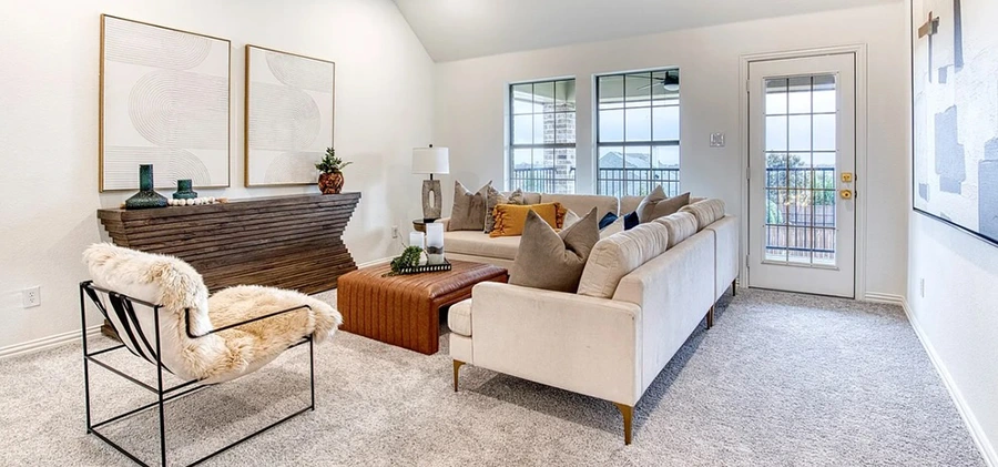 Seating area with large light tan shaped sofa with dark tan and cognac pillows, a side chair and modern console table with two large abstract art pieces above.