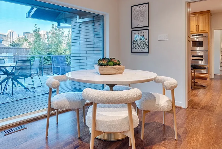 Small dining area with a round marble table with a gold base, four white boucle chairs, and greenery on the table