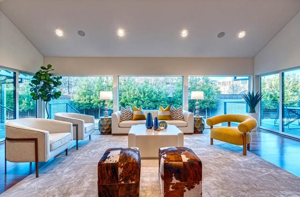 Living room staged in Dallas texas with a white sofa and gold and geometric pillows, two white side chairs, a yellow side chair and two rawhide ottomans