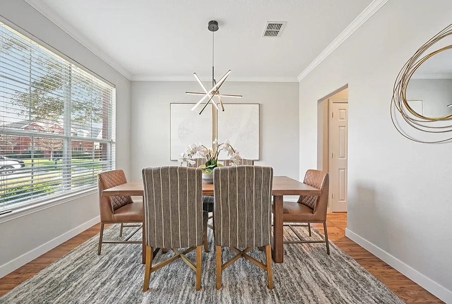 Bright dining room with a large rectangular wood table, two leather end chairs, four stripped side chairs and two white abstract pieces of art