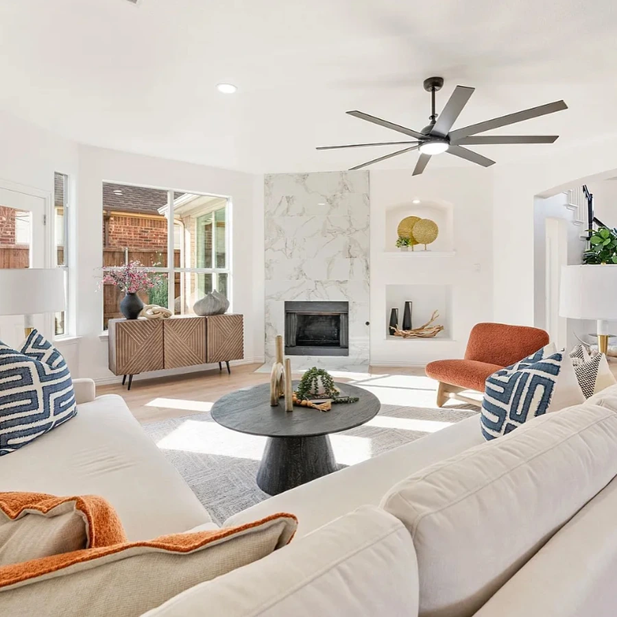 Bright living room with white L-Shaped sofa with orange and blue pillows, a matching orange side chairs and a light wood console table