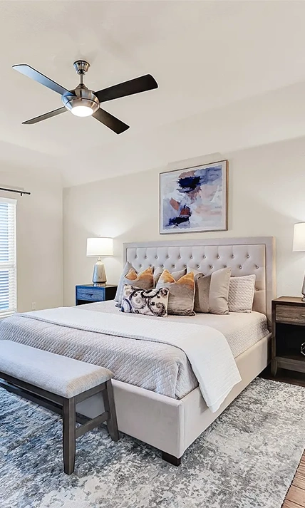 Bedroom with grey upholstered bed, grey bench, grey white and tan pillows and artwork