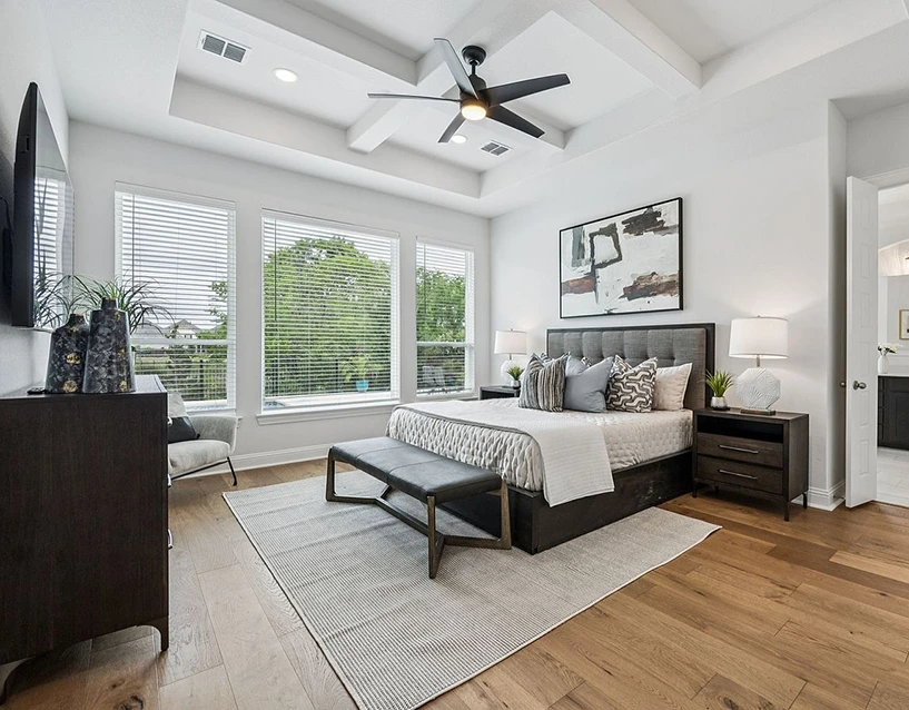 Staged bedroom with a dark wood bed with a grey upholstered headboard, black leather bench, dark wood nightstands and large abstract artwork
