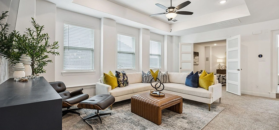 Seating area staged with a large white l-shaped sofa, leather ottoman and a modern dark wood chair and matching ottoman