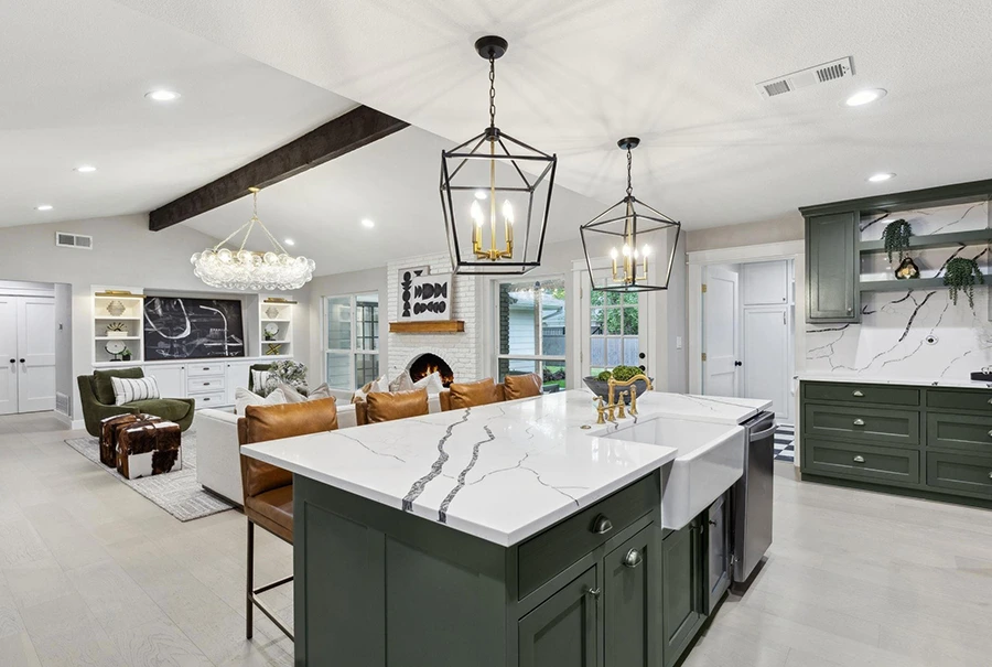 View from a staged kitchen island with quartz countertops looking toward an open-concept living space with a white brick fireplace and a bubble-glass chandelier