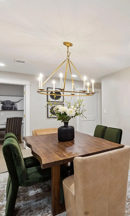 Staged dining table vignette featuring a black vase with white flowers, green velvet chairs, and a gold candle chandelier