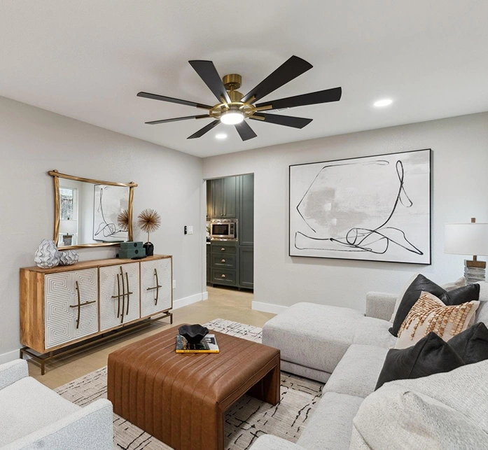 Staged living room corner with a light grey sectional, a geometric wood sideboard with gold accents, a cognac leather ottoman, and a black abstract painting