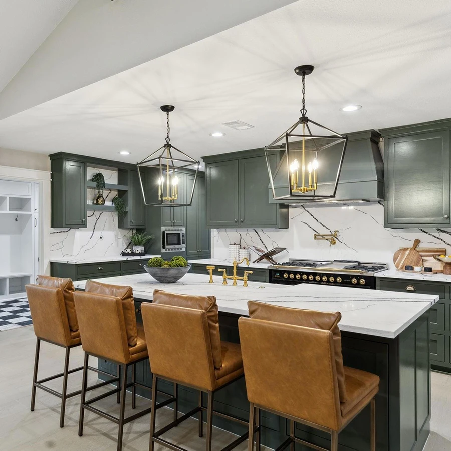 Long view of a staged luxury kitchen island lined with four tan leather barstools under black metal lantern chandeliers