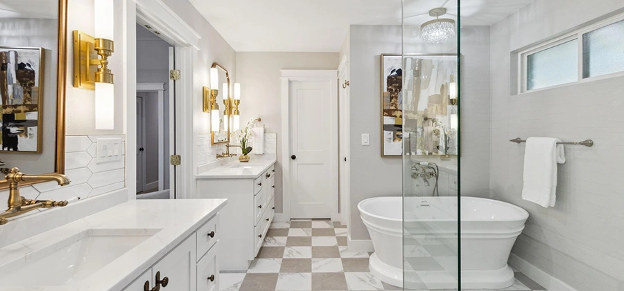 Staged luxury bathroom featuring a standalone soaking tub, dual white vanities with gold hardware, and a grey-and-white checkered tile floor