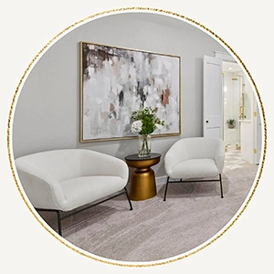Circular vignette of a primary bedroom sitting area with two white bouclé chairs, a gold side table, and a large abstract painting