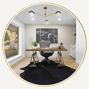 Circular vignette of a staged home office featuring a wooden desk, a grey tufted office chair, a black cowhide rug, and a modern gold light fixture