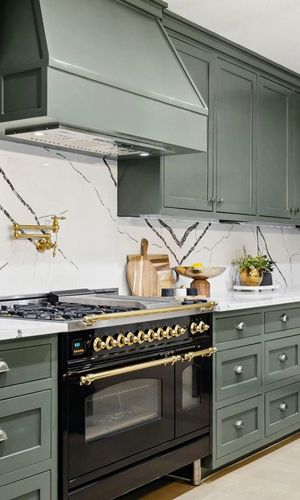 Close-up of a modern luxury kitchen featuring sage green cabinets, dramatic black-and-white marbled quartz backsplash, a black gas range, and gold hardware