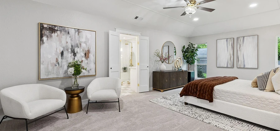 Wide view of a staged luxury bedroom suite including a dedicated sitting area with two white bouclé chairs, gold side tables, and a large abstract painting