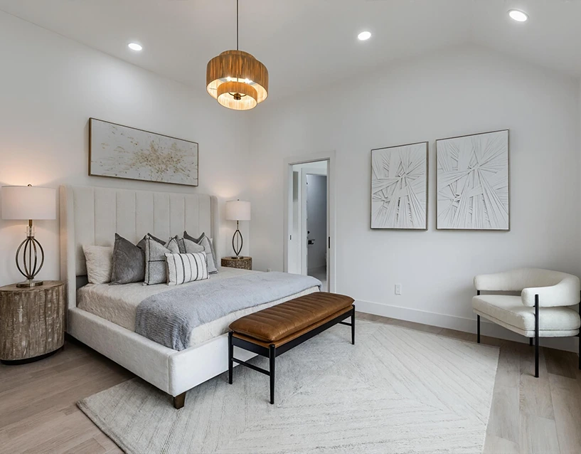 Staged primary bedroom featuring a white tufted wingback bed, textured neutral bedding, a tan leather bench, and a modern tiered wood chandelier