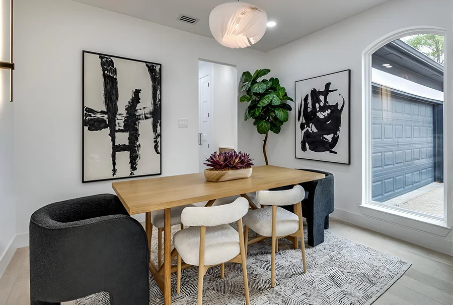 Staged modern dining room with a light wood table, white bouclé chairs, dark upholstered armchairs, and two large black-and-white abstract paintings
