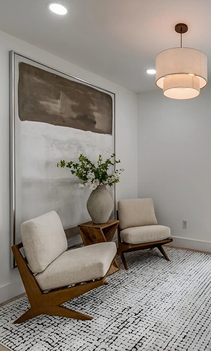 Neutral home staging vignette featuring two wood-frame bouclé accent chairs, a geometric side table, and a large minimalist color-block painting