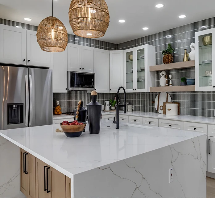 Staged contemporary kitchen with a large quartz waterfall island, light wood lower cabinets, white upper cabinets, and a grey vertical matchstick tile backsplash