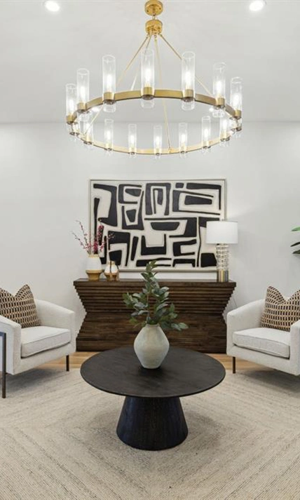 Seating area with two white boucle arm chairs, small round black table, a modern wood sideboard and large black and beige art