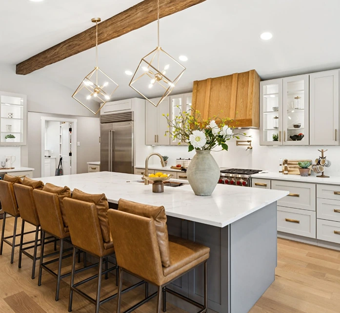 Staged kitchen with four camel colored leather barstools, two gold square pendant lights and kitchen accessories