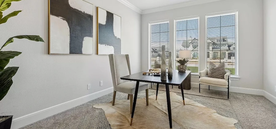 Home office staged with a black desk, grey high back chair, rawhide rug, and two white and black abstract art