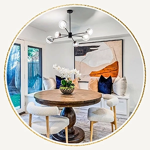 Dining area staged with a round wood table, three white boucle chairs, a seating bench with white, blue and tan pillows 