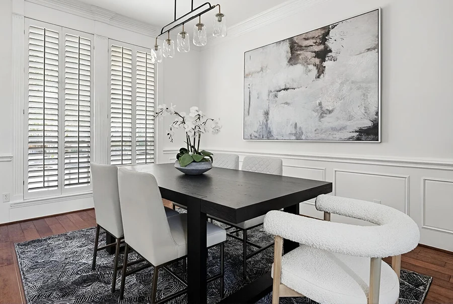 Dining room staged with a black dining table, six white leather chairs, and neutral beige and white abstract artwork