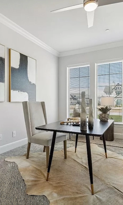 Modern home office with a black table, grey winged back chair, rawhide rug and two black and white abstract pieces of art.