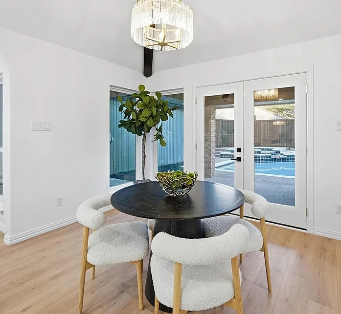 Dining room with a round black table, four white boucle chairs with light colored wooden legs and doors that open to the back pool area