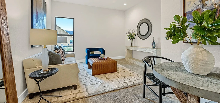A small seating area with a tan sofa, blue velvet swivel chair, cognac leather ottoman and a small table with two chairs