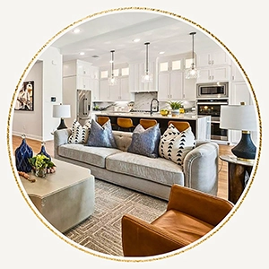A circular photo showing the seamless flow from a neutral-toned living room into a modern kitchen with white cabinetry and cognac leather barstools.