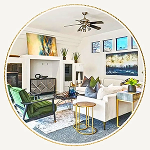 A seating area with a large white l-shaped sofa, two green velvet chairs, a black and white console table and coloful artwork.