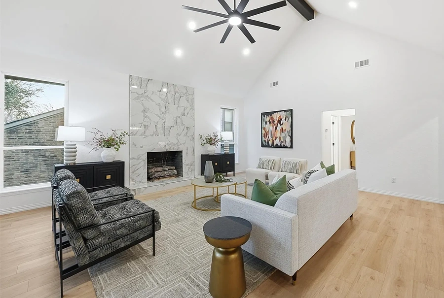 modern living room with high ceilings, white and grey marble fireplace, white sofa with green pillows, two black textured chairs and two white velvet chairs.