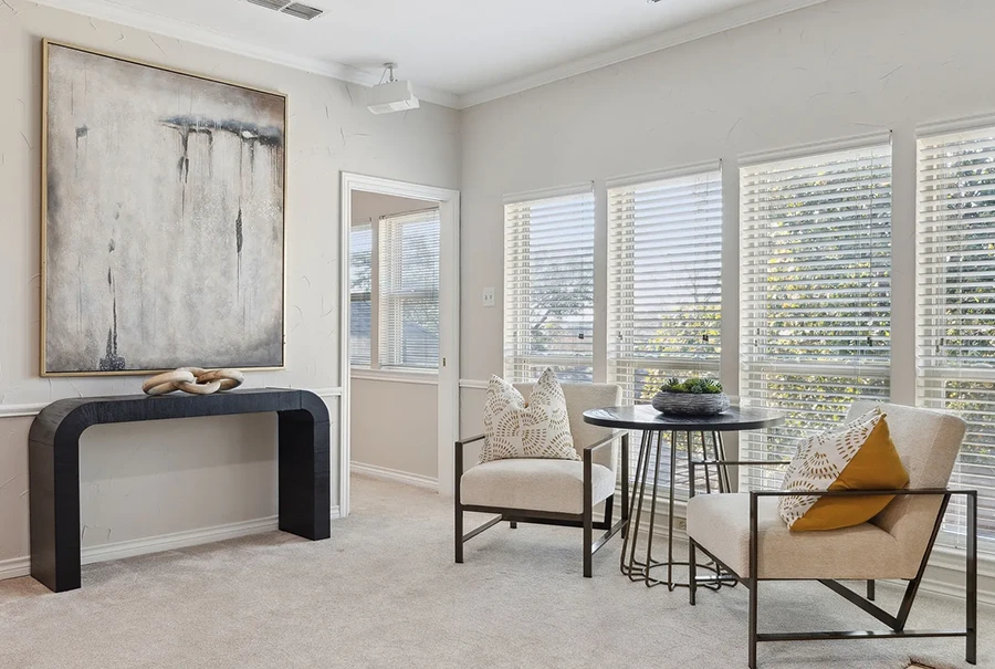 Staged seating area with two metal frame chairs with white cusions, round accent table and wooden console with large modern artwork