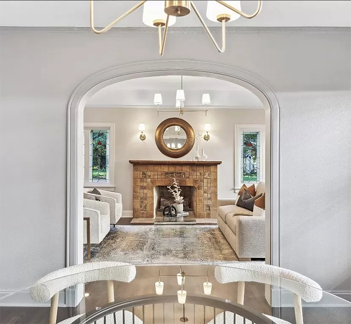 A view from behind two white armchairs looking through an archway toward a fireplace, emphasizing the symmetry and open layout of the home.