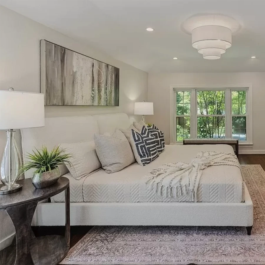 Bedroom with a white upholstered bed, blue and white bedding, vertical abstract artwork above the bed and large windows