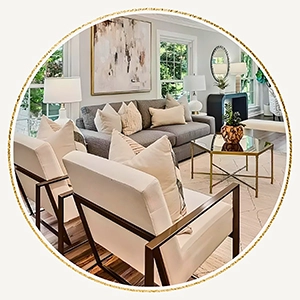 A circular photo featuring a grey sofa with cream pillows and two white modern armchairs with dark metal frames arranged around a hexagonal glass coffee table.