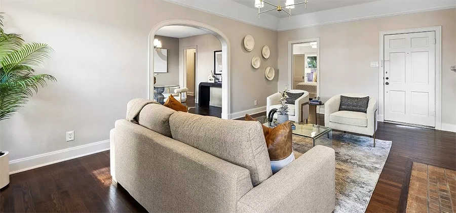 A wide-angle view of a living room flowing into a dining area, showing neutral furniture and large arched doorways that highlight the home's architectural flow.