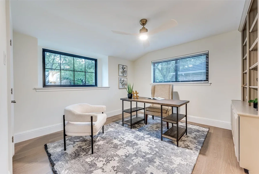 Staged home office featuring a wooden desk with open shelves, a cream barrel chair, and an abstract grey-and-white area rug