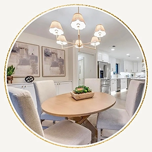 Circular vignette of a casual dining area featuring a round light-wood table, cream chairs, and a shaded gold chandelier