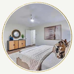 Circular vignette showing a staged bedroom with a neutral bed, textured pillows, a wood-and-black console table, and a round mirror