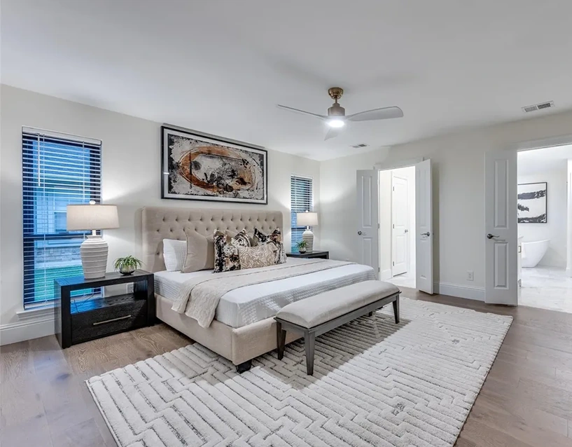 Staged primary bedroom with a tufted cream headboard, geometric patterned rug, and a modern white-and-black abstract painting