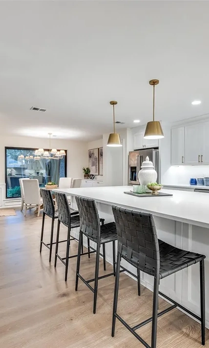 Close-up view of a white kitchen island lined with four black woven leather barstools under gold pendant lights