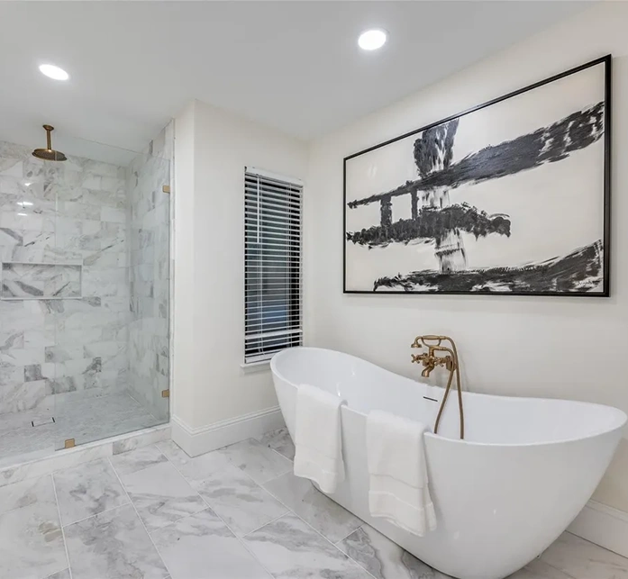 Staged modern bathroom featuring a white freestanding soaking tub, gold fixtures, marble tile, and a large walk-in glass shower