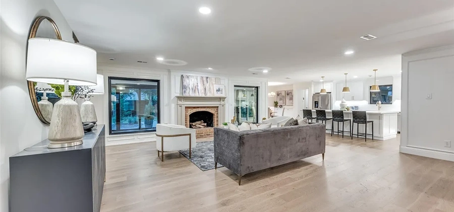 Wide view of a staged living room with a brick fireplace, a velvet sofa, and a large console table with a round mirror