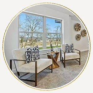 Circular graphic frame showcasing a cozy sitting area with two cream accent chairs, bold black-and-white graphic pillows, and woven basket wall decor