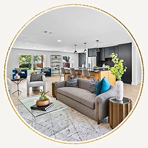 Circular graphic frame showcasing a wide open living room with a grey mid-century modern sofa, teal velvet pillows, and a large dark gray kitchen in the background